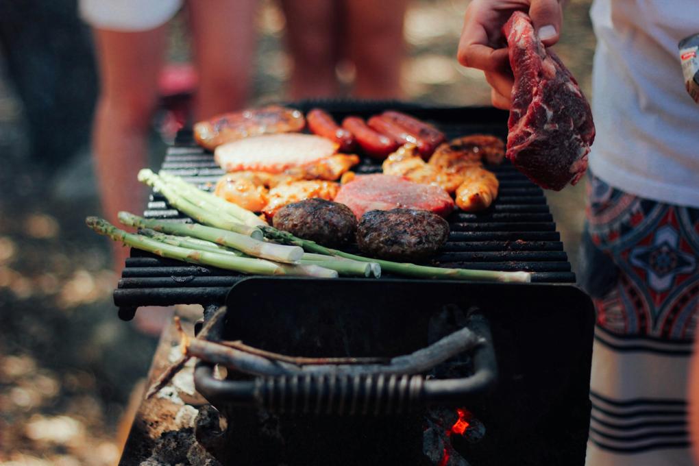 A person barbecues meat and vegetables at an outdoor party