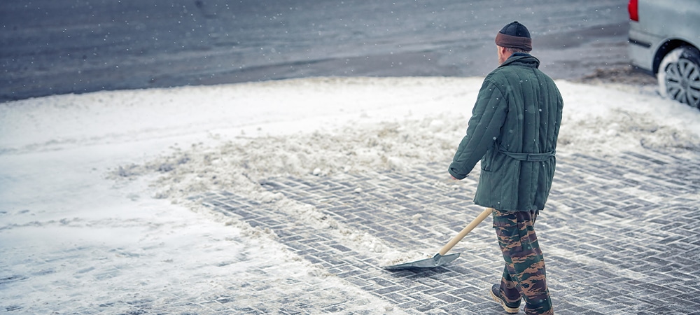 person removing snow using shovel in front of home